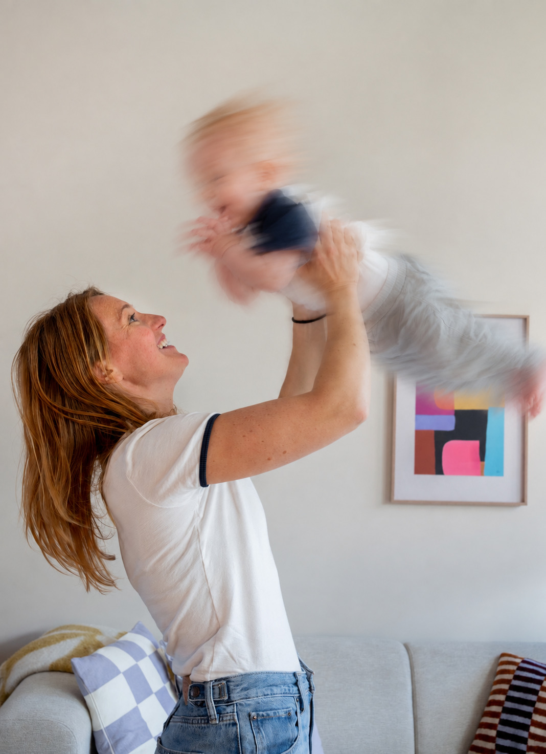 Alieke tilt haar baby lachend hoog de lucht in.